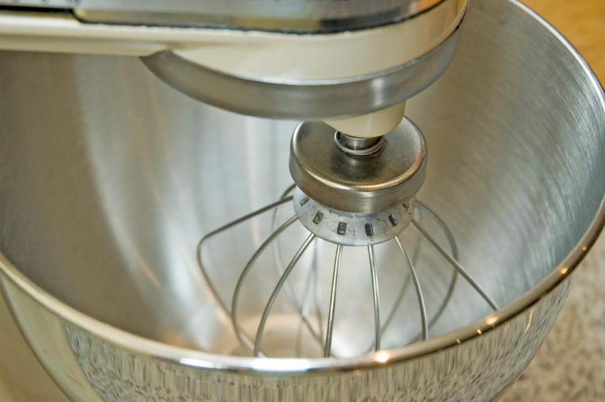 A kitchen mixer with a whisk in a steel bowl